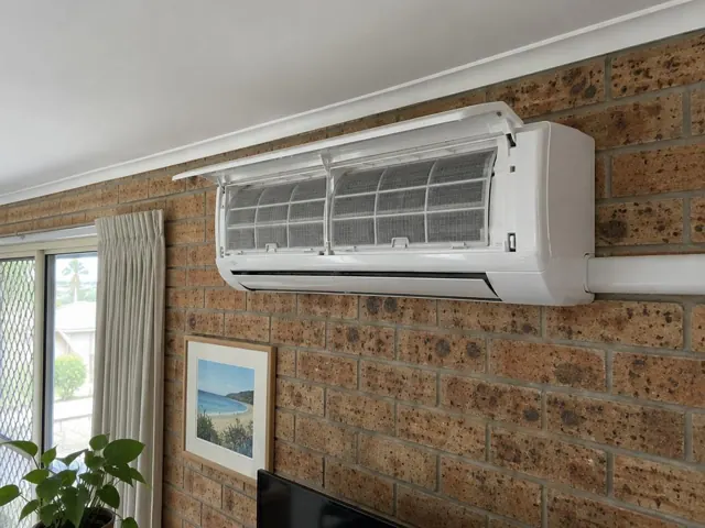 Clean split system indoor head open on a brick wall above a living room in Tugun