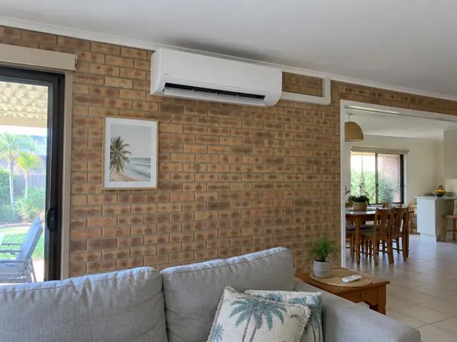 Split system on a brick wall above a living room couch, with open louvre and neat piping in Palm Beach